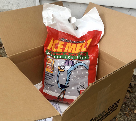 An open cardboard box showing a bag of ice melt inside